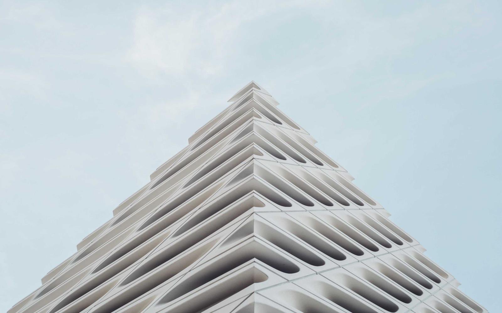 Looking up at a sculpted white concrete pavilion against open sky